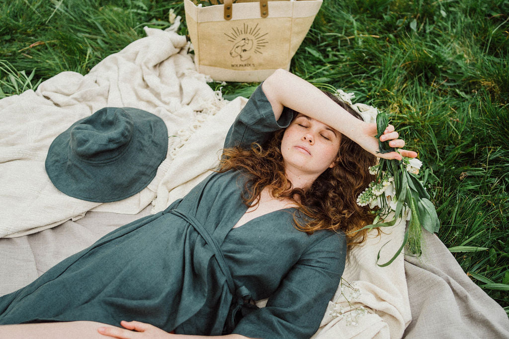 Solpardus relaxing picnic in field in Mawnan Smith Cornwall. Delphi linen dress Nyx linen hat Solpardus logo jute bag. All natural ethical sustainable sunwear linen clothing perfect for sensitive skin psoriasis and eczema