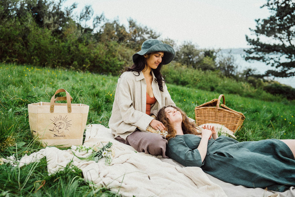 Solpardus picnic with friends in wild field in Mawnan Smith Cornwall. Solpardus logo jute bag, Nyx linen hat, Saba linen shirt, Thea bamboo onepiece, Atti linen trousers, Delphi linen dress. All natural ethical sustainable sunwear swimwear linen clothing perfect for sensitive skin psoriasis and eczema